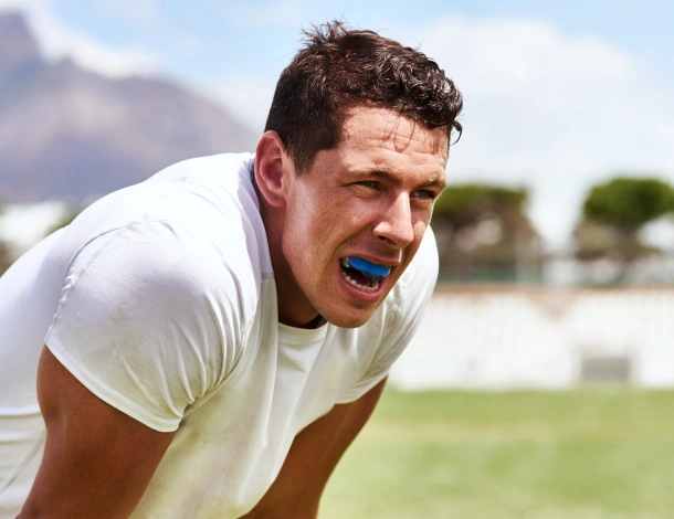 Athletic man wearing mouthguard on sports field, demonstrating dental protection during physical activity.