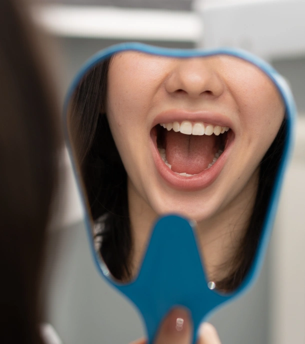 Woman smiling broadly at dental mirror, showing teeth in clinical setting.