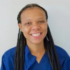 Professional headshot of smiling female dental associate wearing blue scrubs against neutral background.
