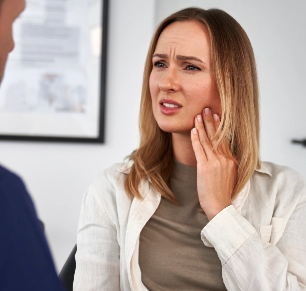 Woman in dental office touching her cheek, appearing to experience tooth pain or discomfort.