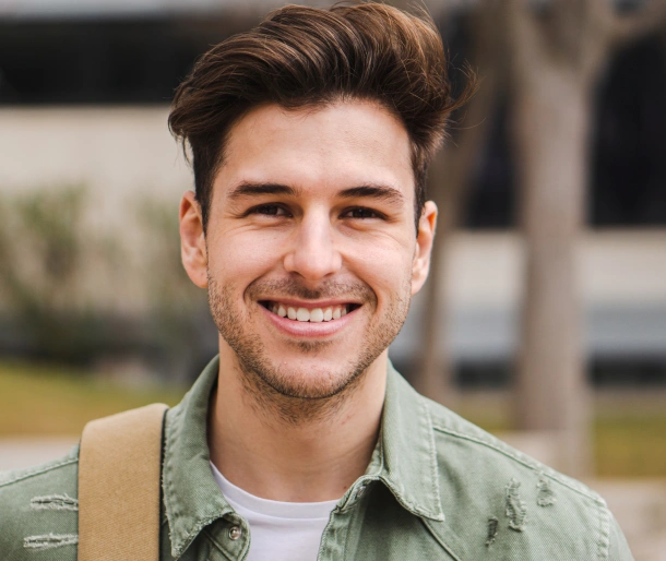 Young man smiling at camera wearing green shirt outdoors near building