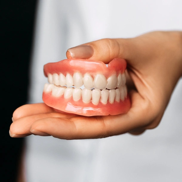 Hand holding a complete denture model displaying artificial teeth against a blurred background.