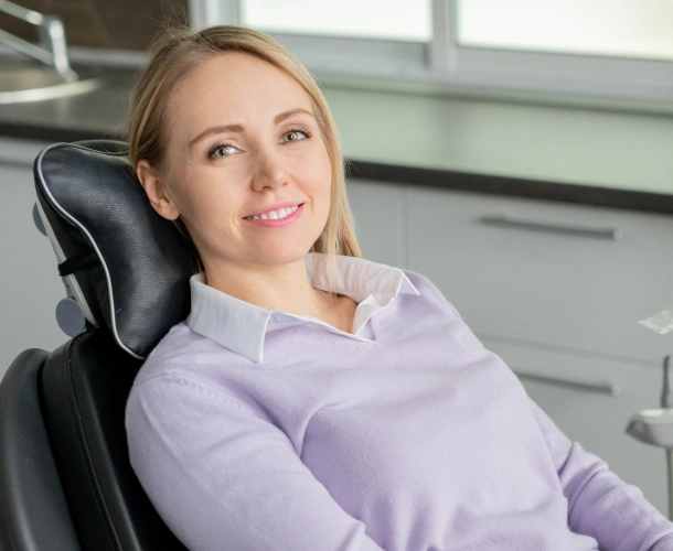 Woman in lavender blouse seated in dental chair at modern office setting.