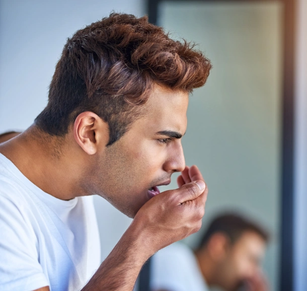 Man in white shirt with hand to mouth, appearing thoughtful or concerned in dental office setting.
