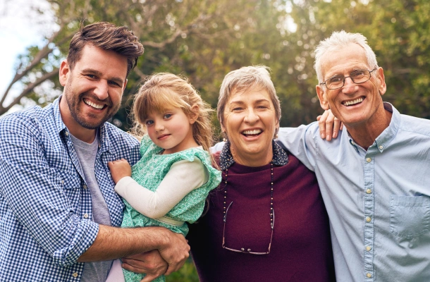 Four generations family smiling outdoors together in natural setting with trees