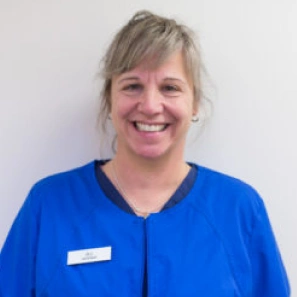 Smiling dental professional in blue scrubs wearing name badge against white background.