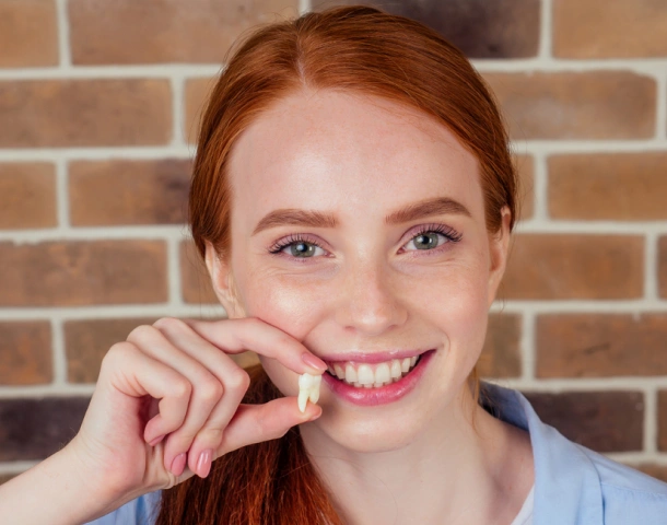 Young woman with red hair smiling while holding dental floss against brick wall background.