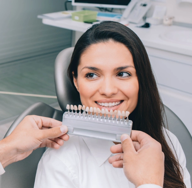 Woman holding dental shade guide in modern dental office setting, smiling at camera.