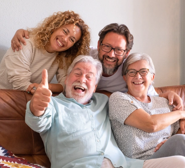Four generations of a family smiling and embracing together on a couch, displaying happiness and togetherness.