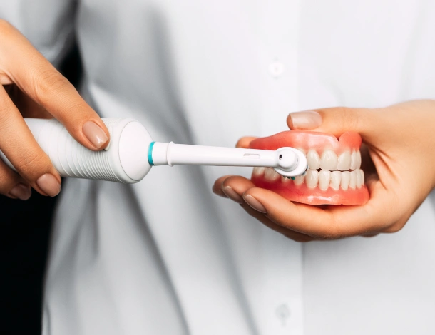 Person demonstrating proper electric toothbrush technique on dental model showing teeth and gums.