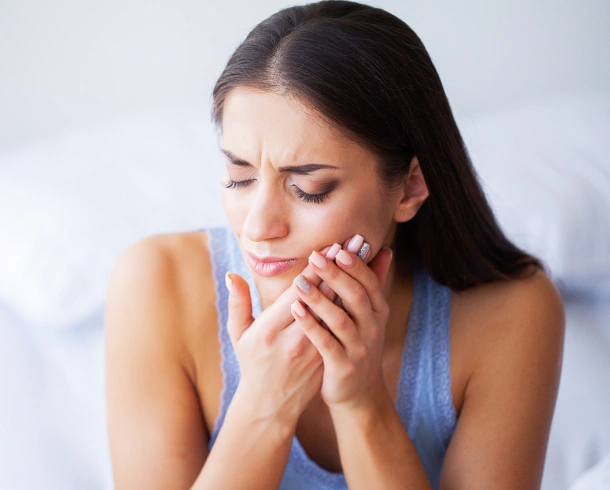 Woman holding face in pain, experiencing dental discomfort in clinical setting.