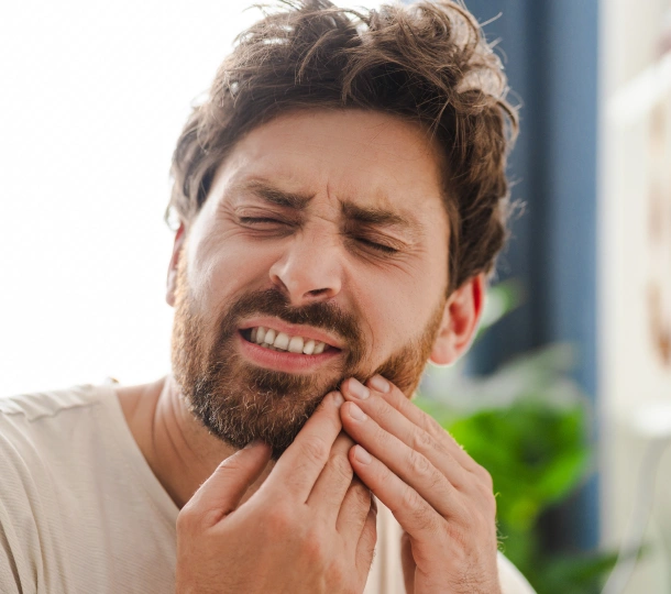 Man with beard experiencing tooth pain, touching jaw, outdoor setting.